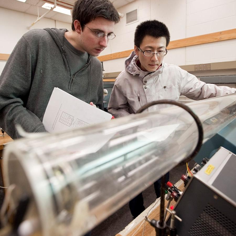 2 students work with a long tube in lab.