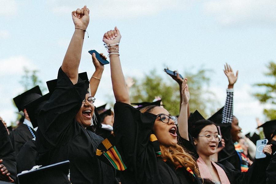 students in cap and gowns raise hands in celebration during commencement